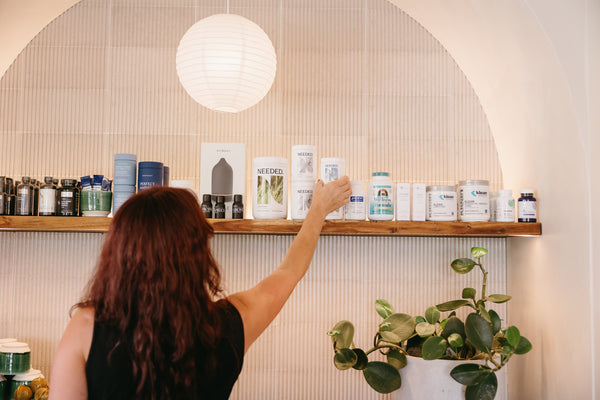 Person reaching for a product on a shelf with various items in a well-lit room.