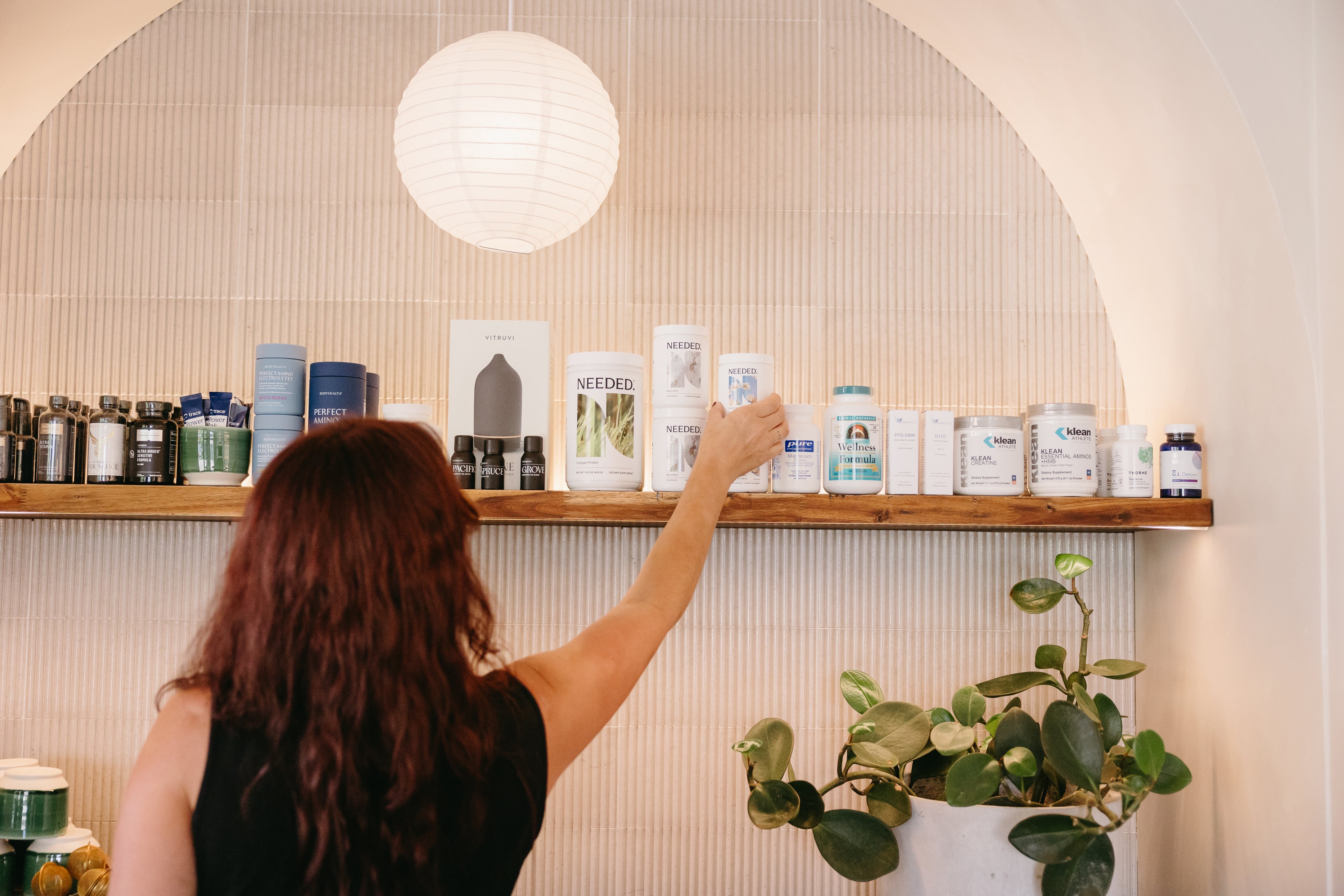 Person reaching for a product on a shelf with various items in a well-lit room.